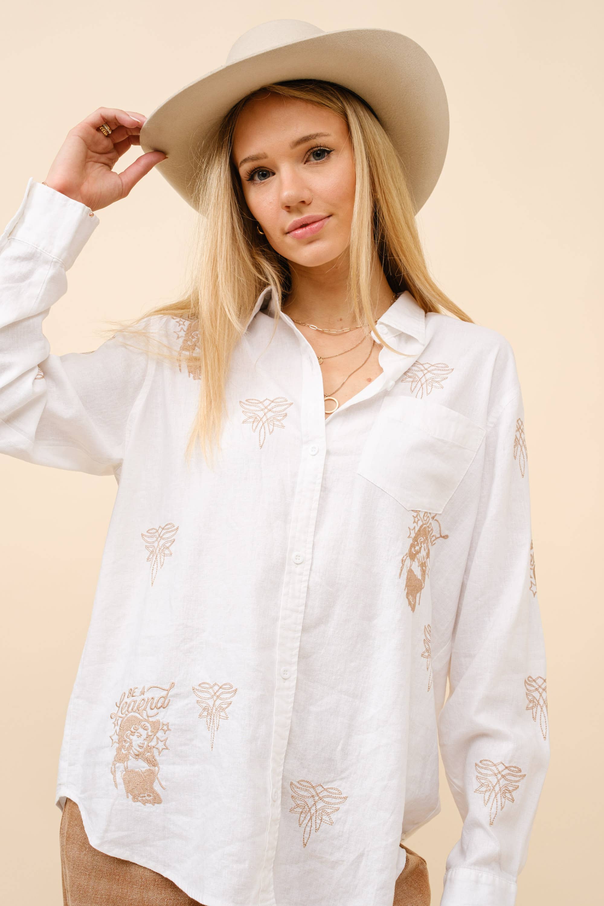 Woman wearing a white embroidered shirt and beige hat against a beige background