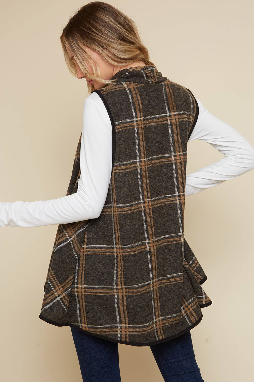 Person wearing a plaid vest over a white long-sleeve shirt on a beige background