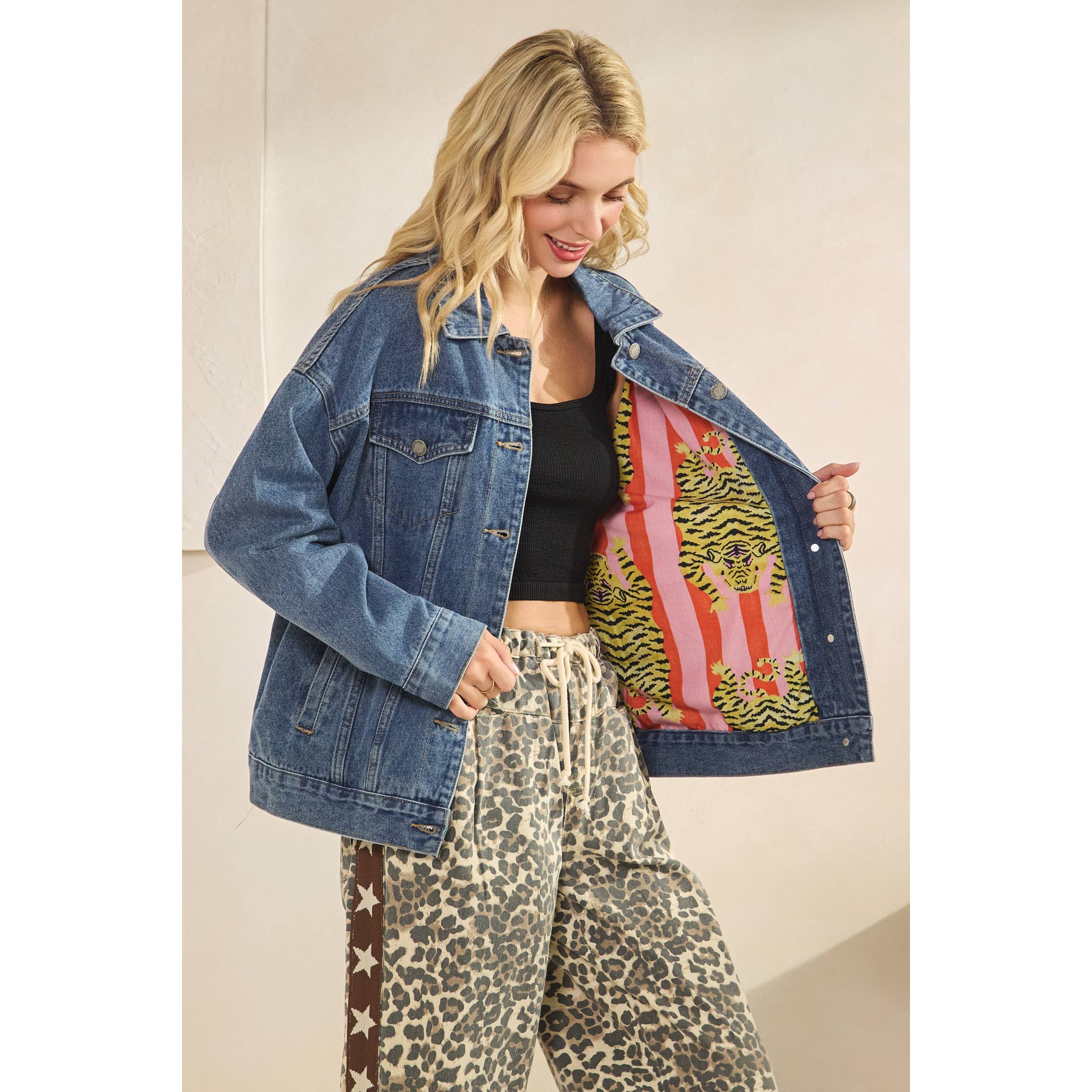 Woman wearing a denim jacket with a colorful patch, black top, and leopard print pants.