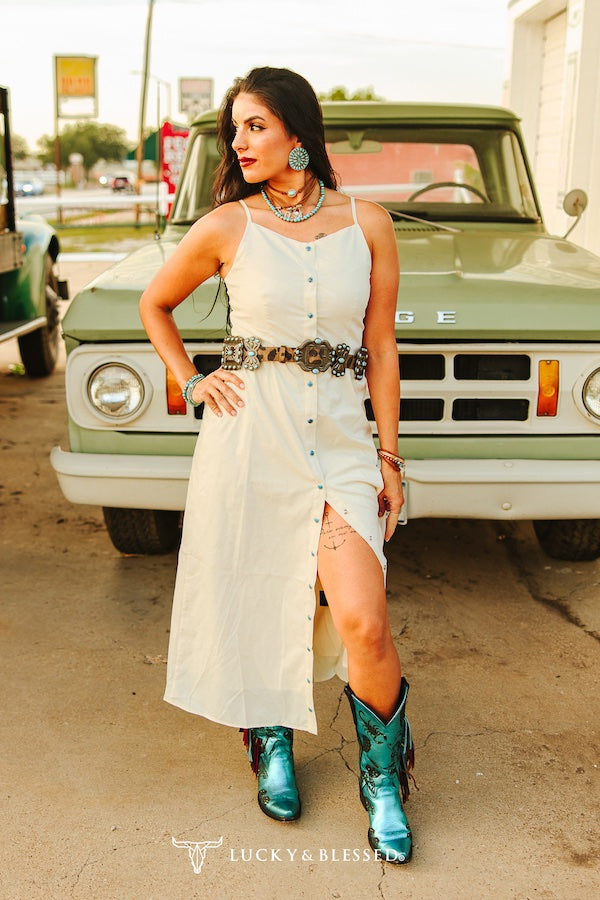 Woman in a white dress and turquoise boots standing in front of a green truck.