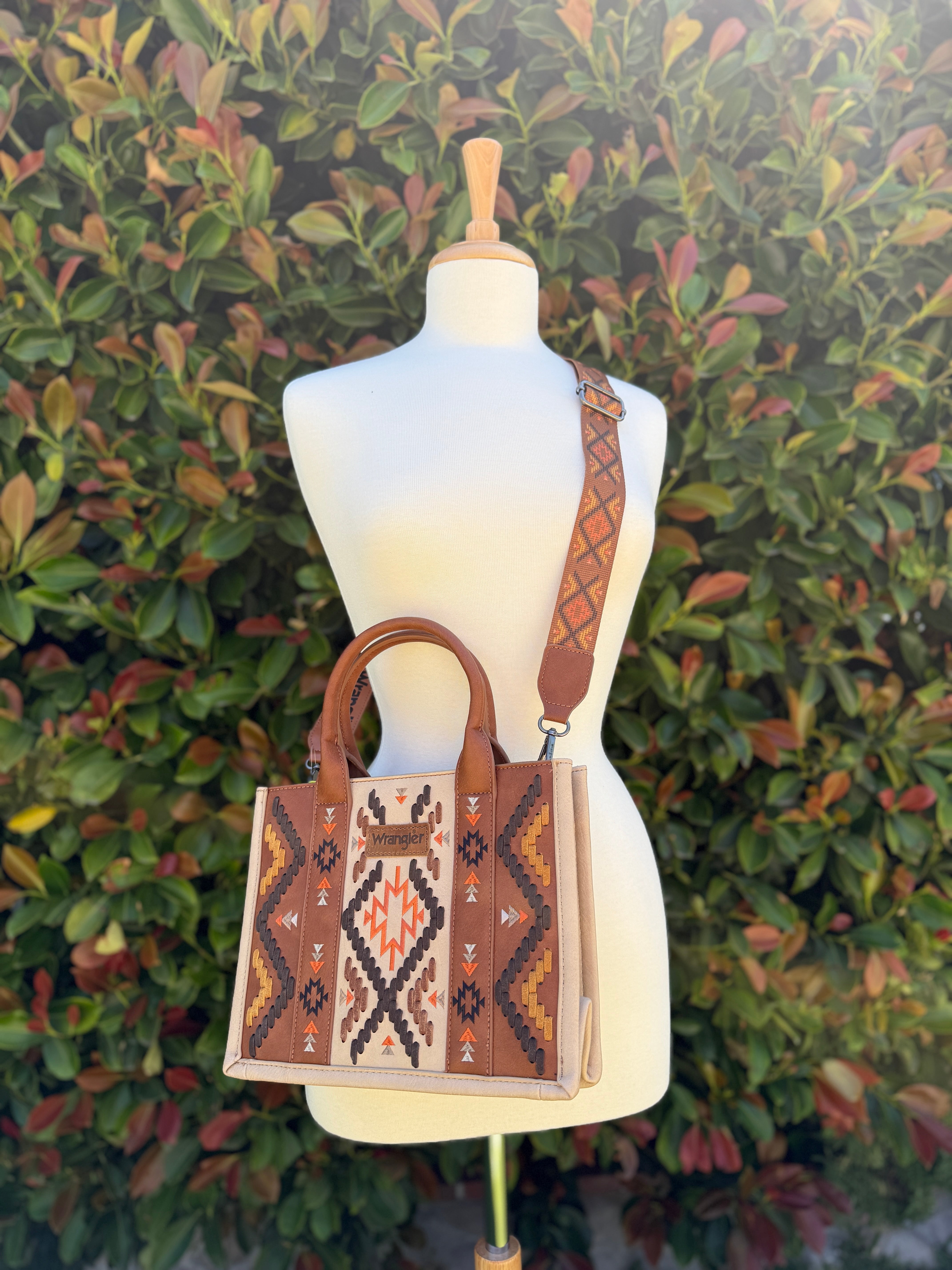 Aztec embroidered tote/crossbody bag in brown, displayed on a mannequin against a leafy background.
