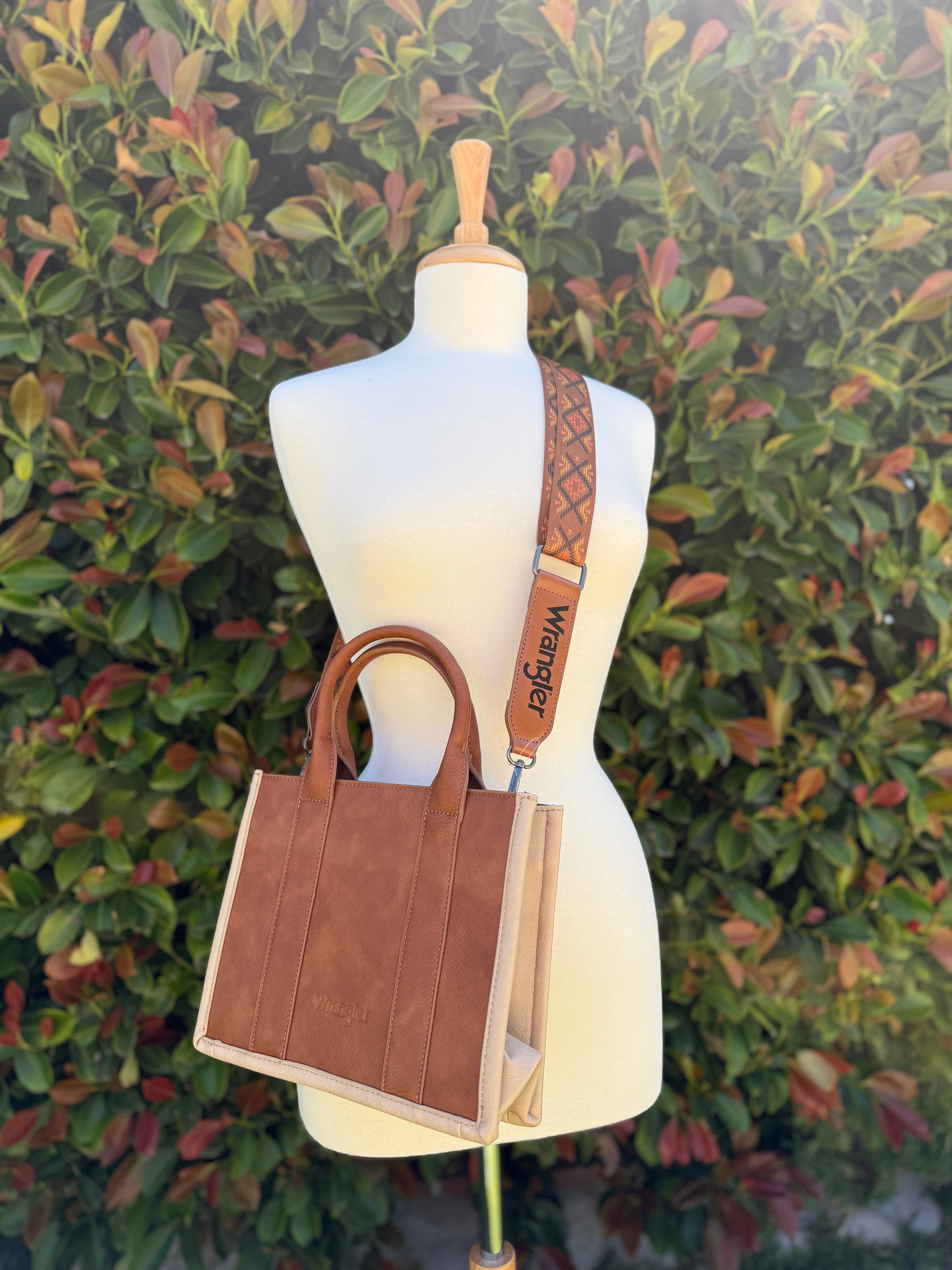 Aztec embroidered tote/crossbody bag in brown, displayed on a mannequin against a leafy background.
