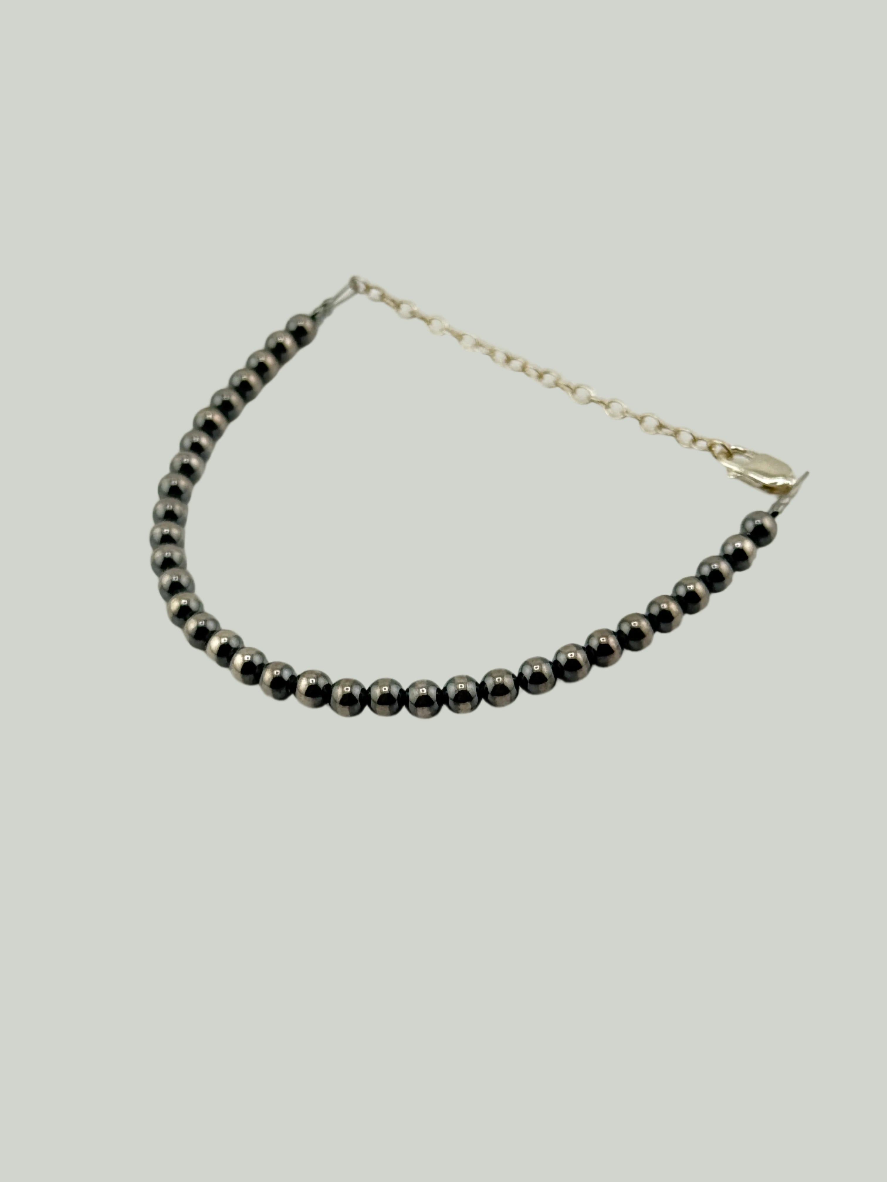 Silver beaded bracelet with silver chain on a light gray background