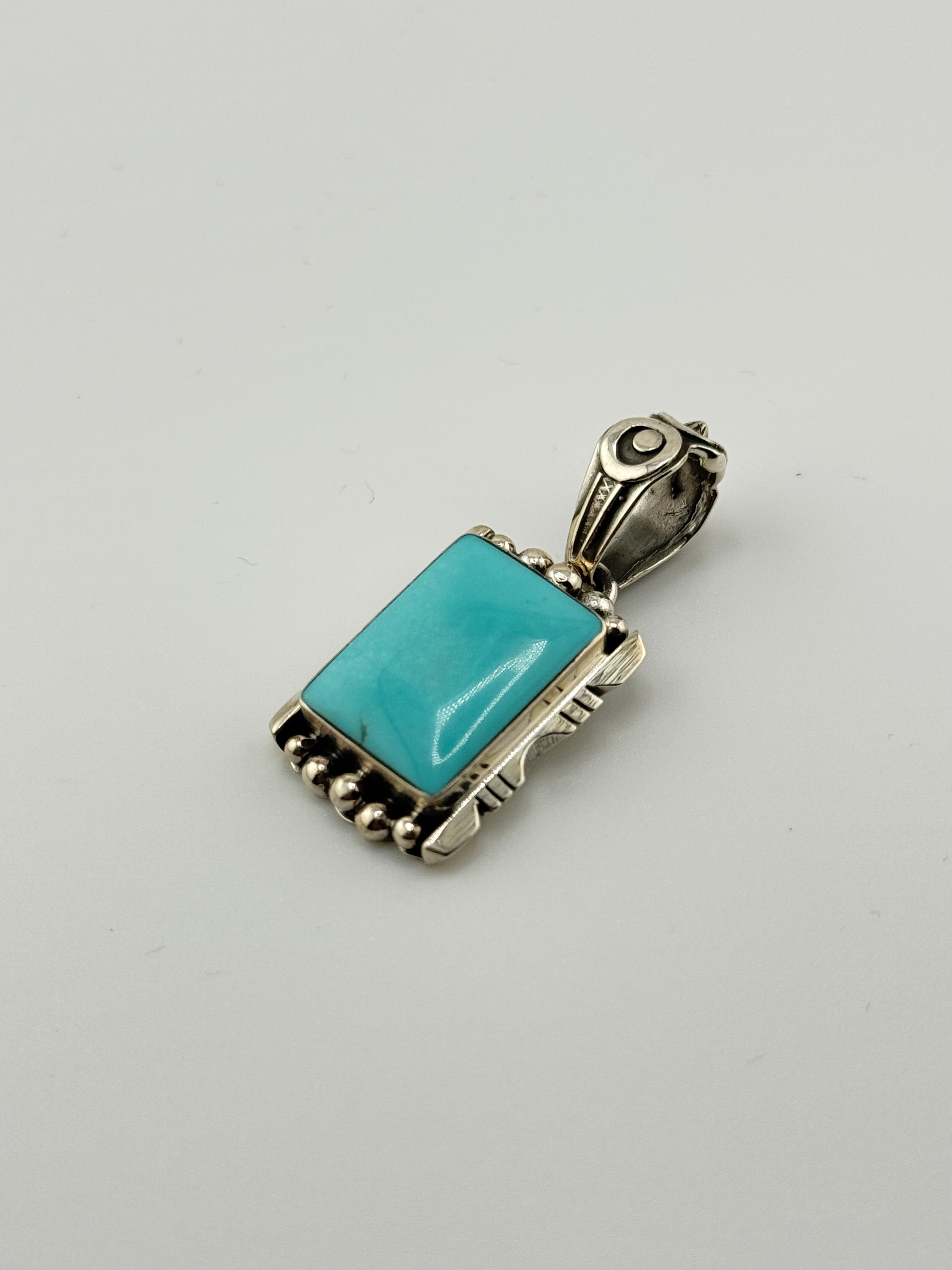 Turquoise pendant with silver frame on a light gray background