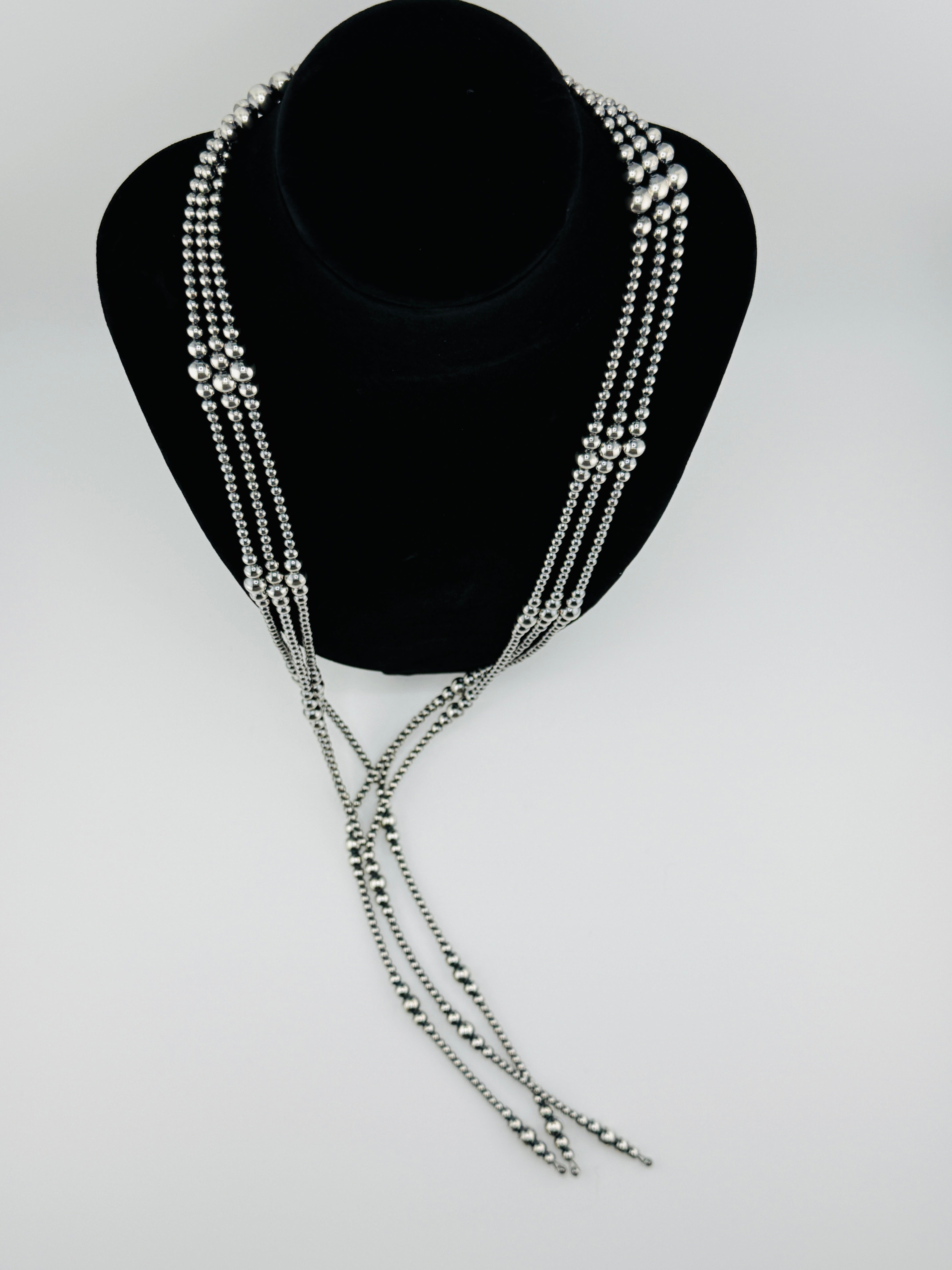 Silver beaded necklace on a black bust against a white background