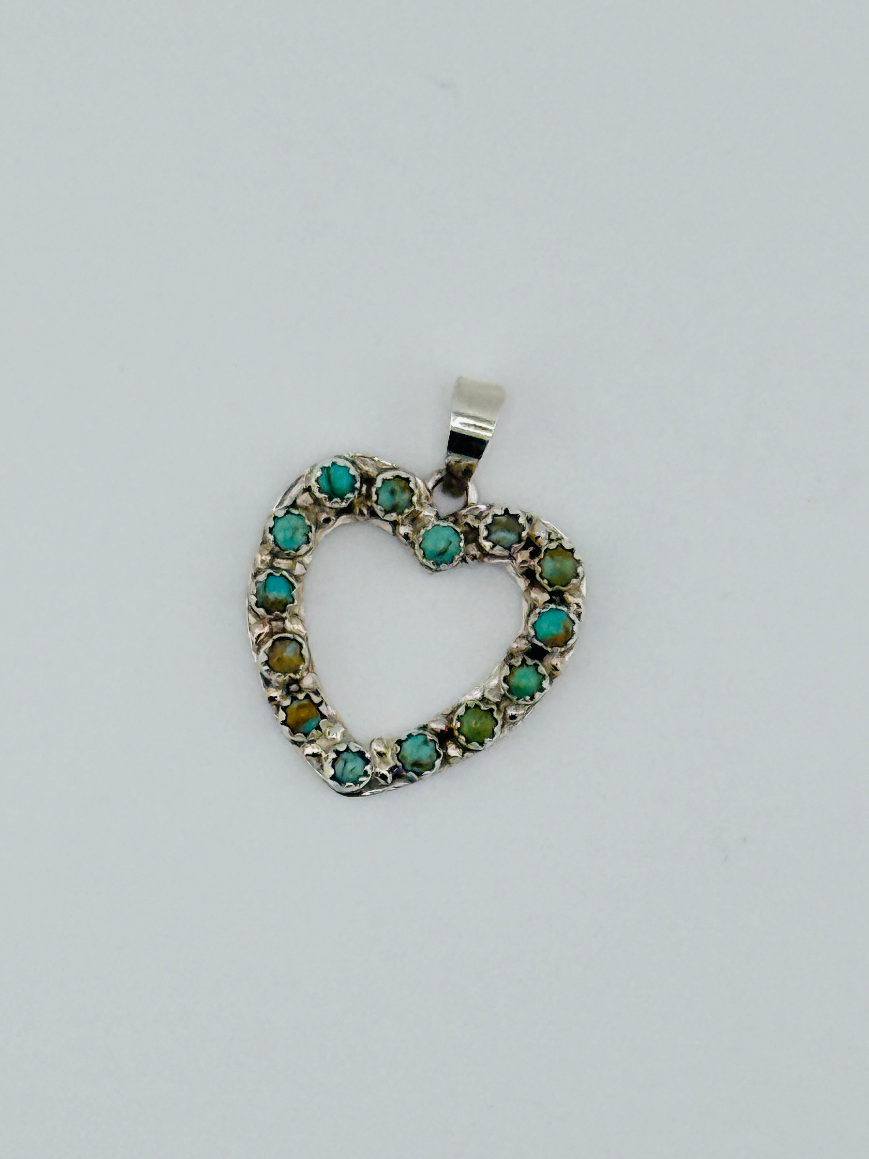 Heart-shaped pendant with green gemstones on a light gray background
