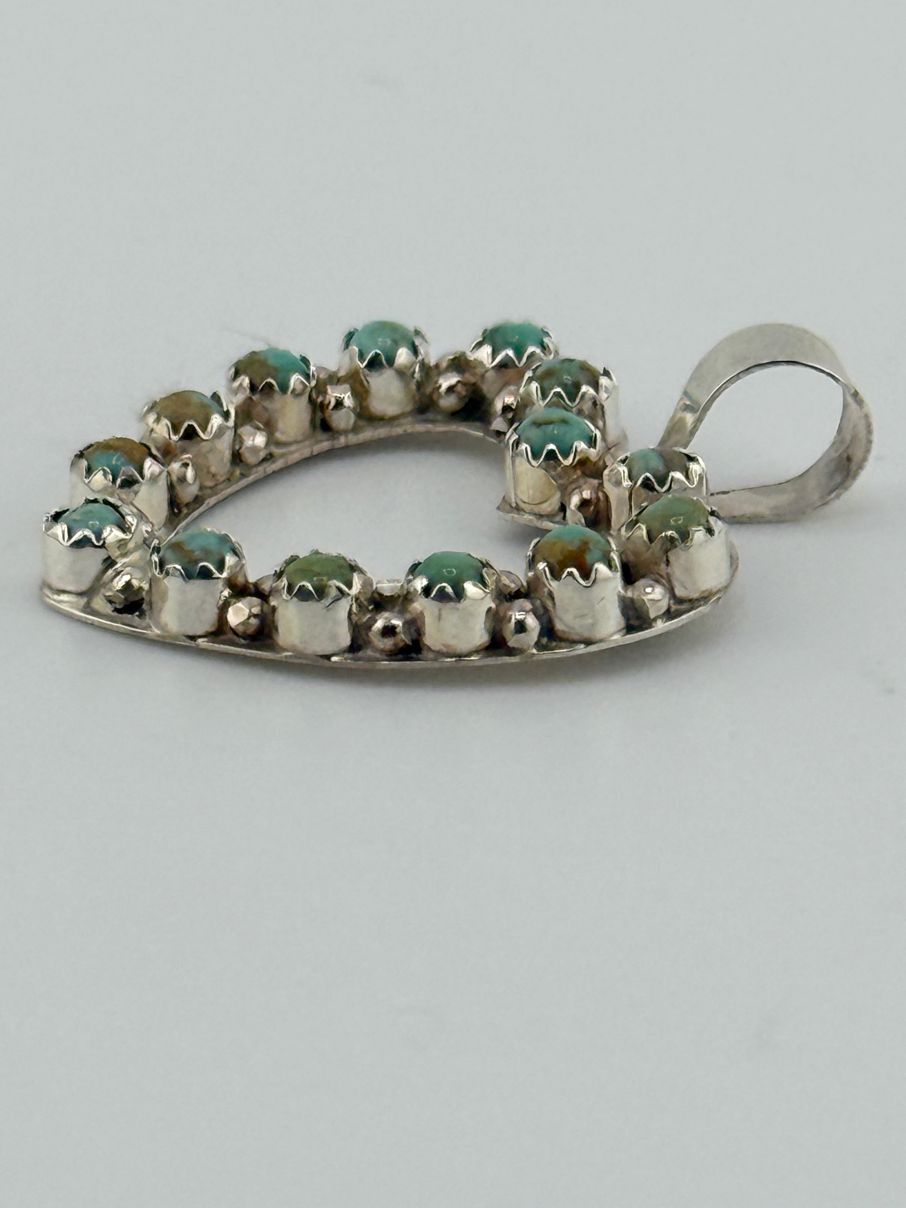 Silver pendant with green gemstones on a light gray background