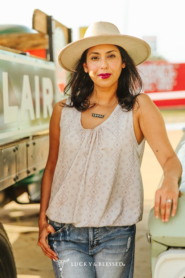 Woman wearing a beige hat and sleeveless top standing next to a vintage truck with 'Lucky & Blessed' branding.