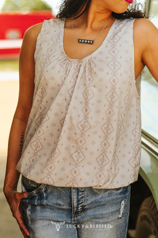 Woman wearing a patterned sleeveless top and jeans with 'Lucky & Blessed' branding.