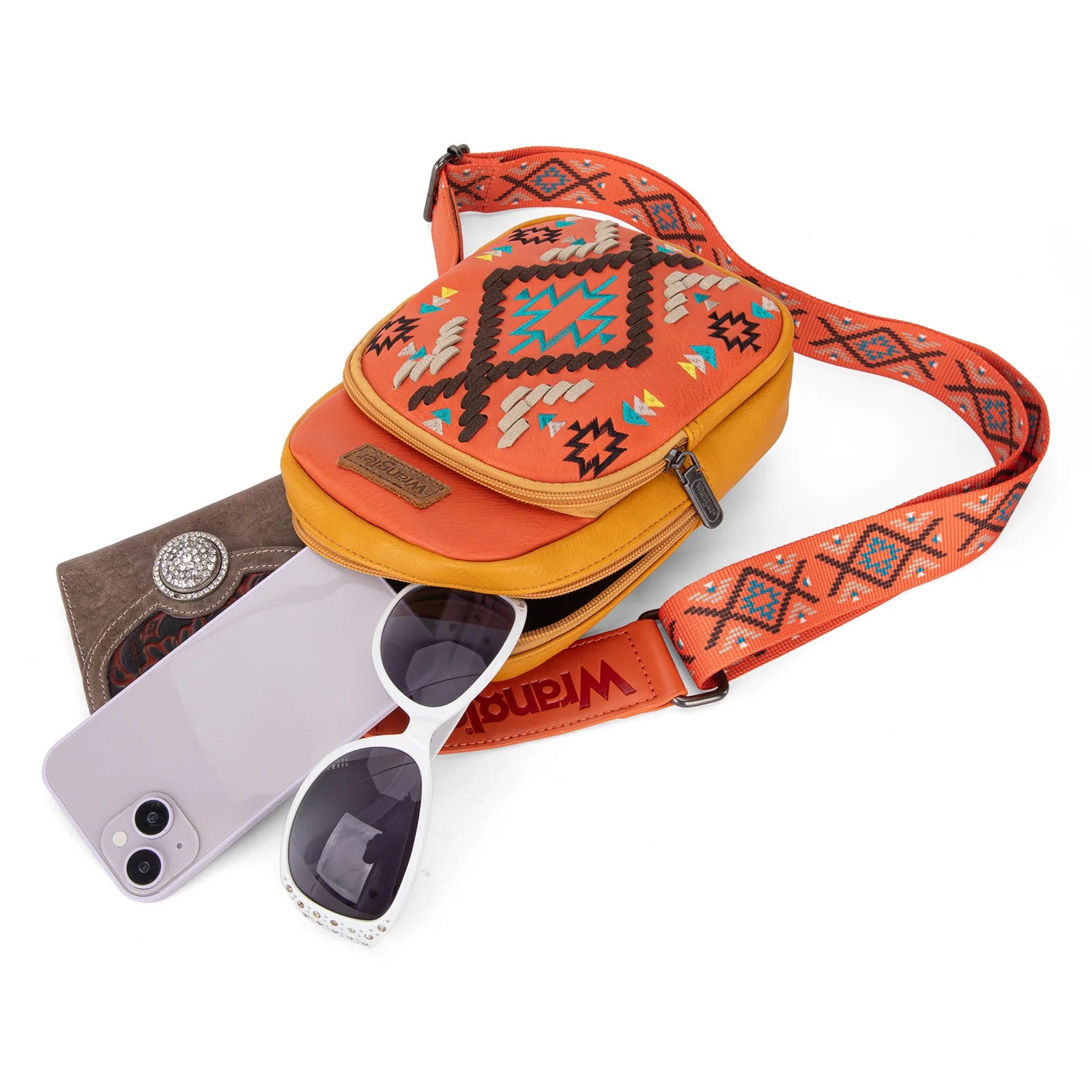 A bright orange and multicolor geometric embroidered Wrangler Southwestern sling bag displayed on a mannequin against a leafy background.