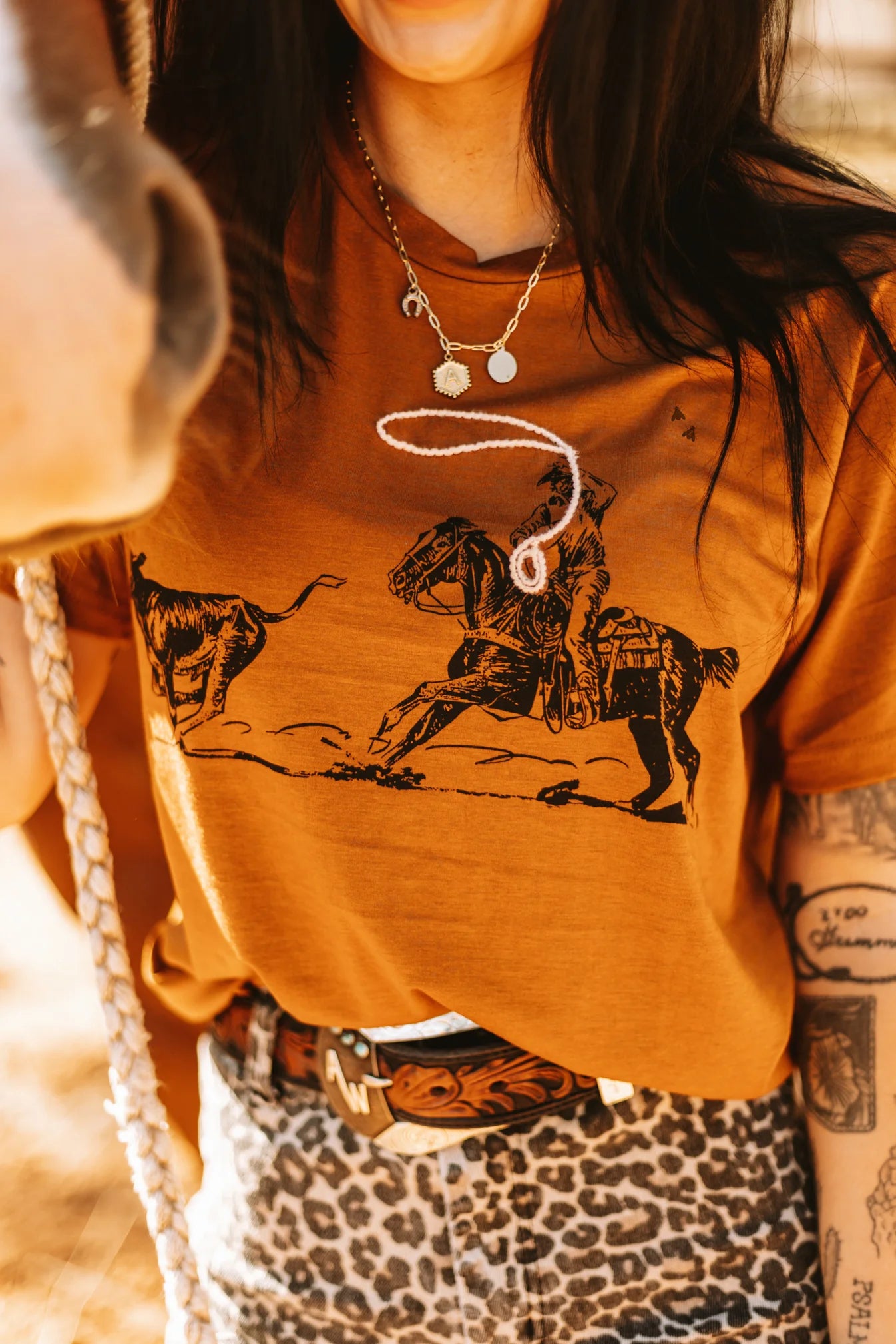A person wearing a brown graphic tee with a horse and rope design, paired with a leopard print skirt and accessorized with a necklace.
