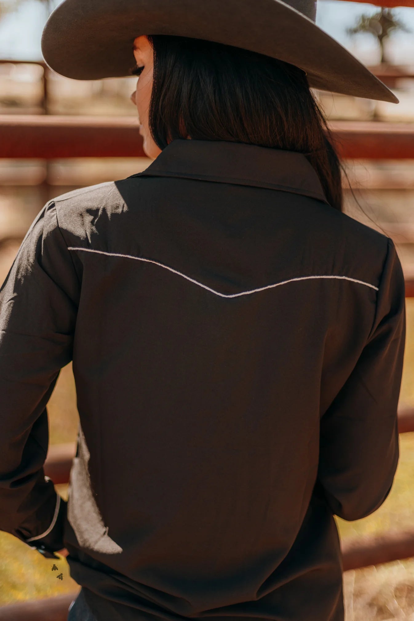 Person wearing a dark shirt and cowboy hat in a rustic setting