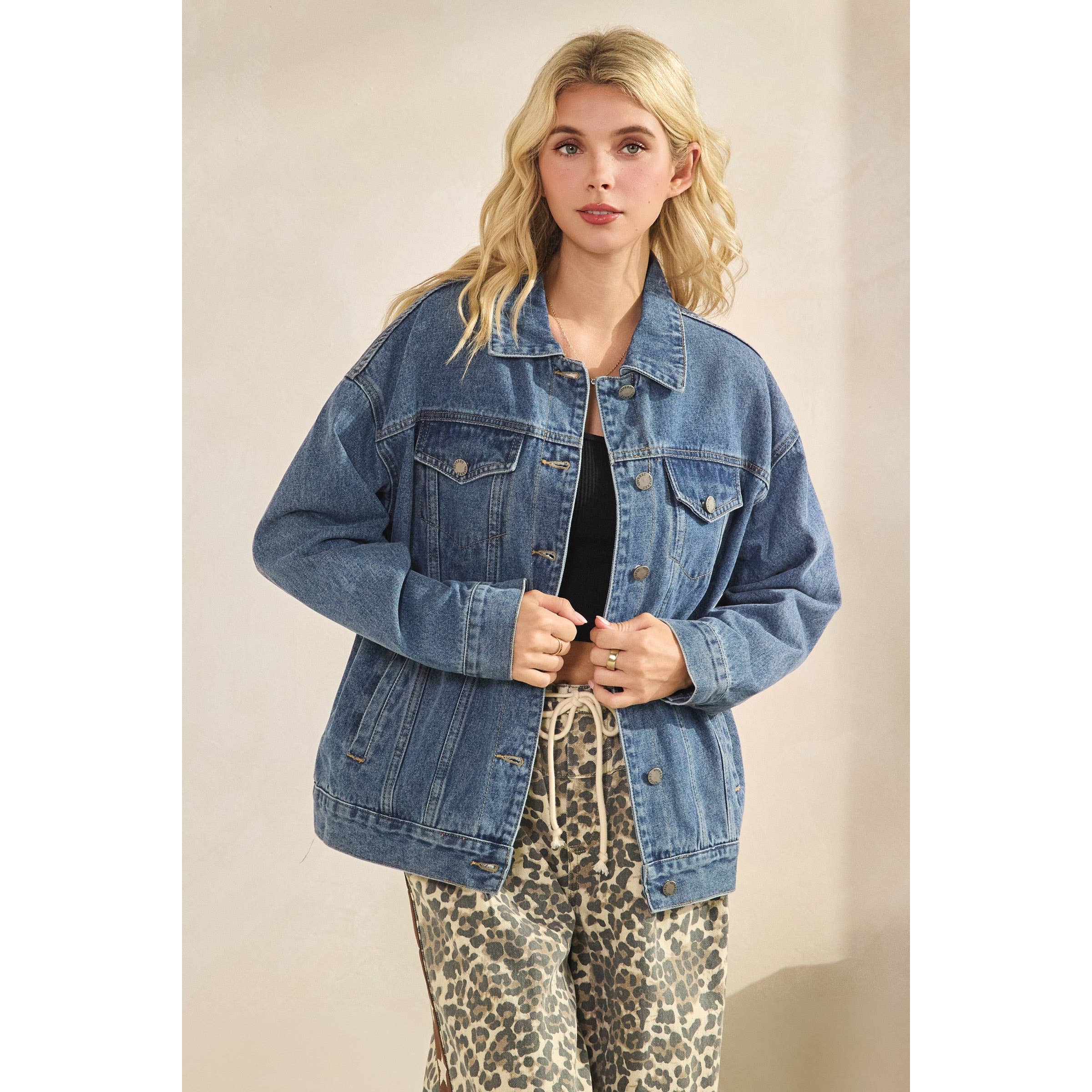 Woman wearing a blue denim jacket over a black top and leopard print pants on a beige background