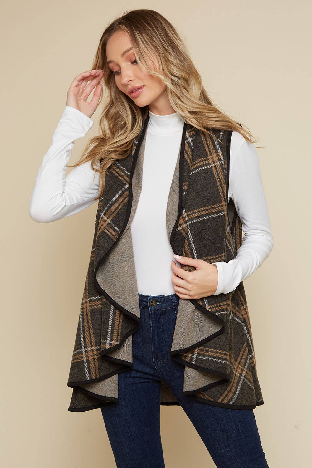 Woman wearing a plaid vest over a white shirt and blue jeans on a beige background