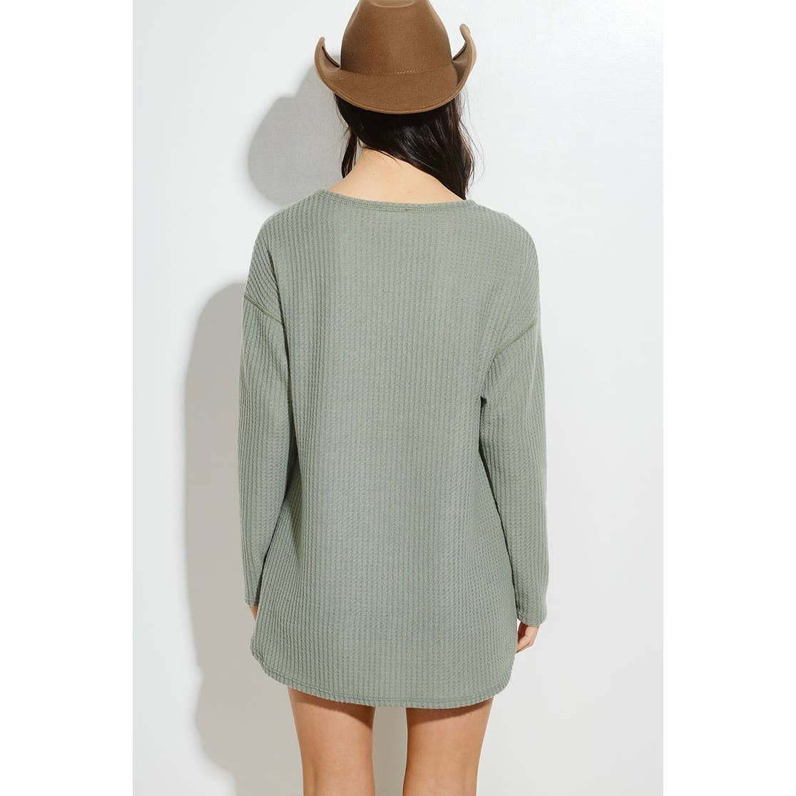 Person wearing a green ribbed sweater and brown hat on a white background