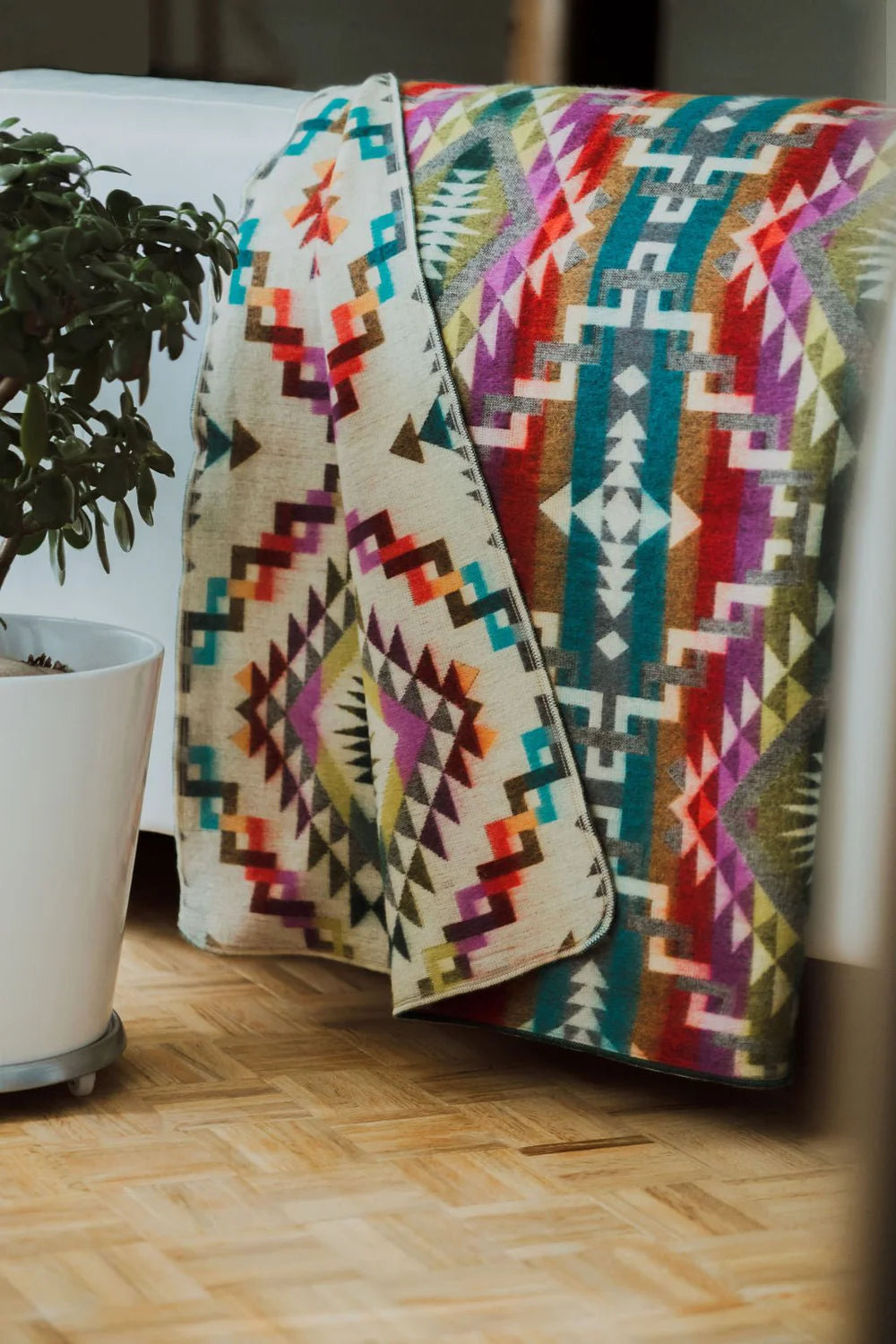 Colorful patterned blanket draped over a chair next to a potted plant on a wooden floor.