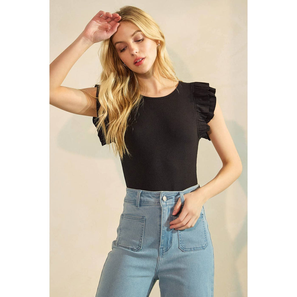 Woman wearing a black top with ruffled sleeves and blue jeans against a neutral background