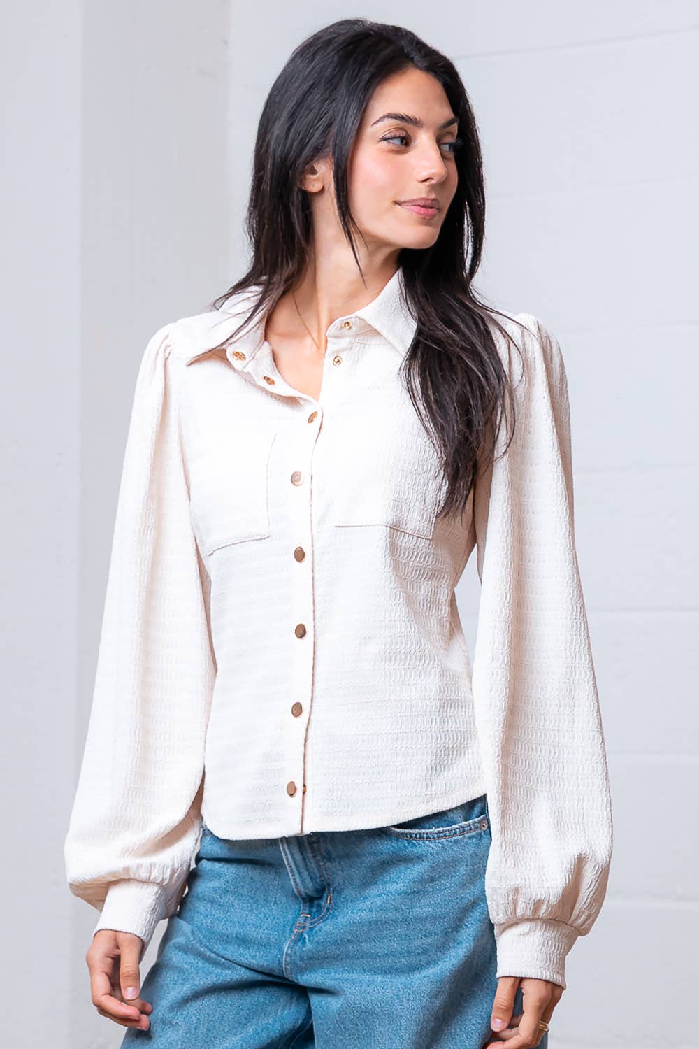 Woman wearing a white blouse with long sleeves and blue jeans against a plain background