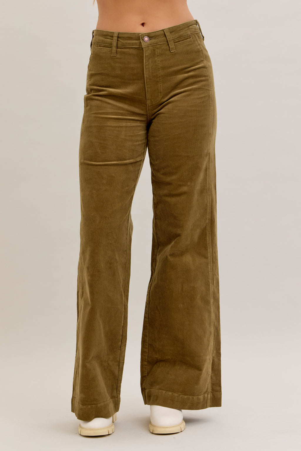 Brown corduroy pants worn by a person on a beige background