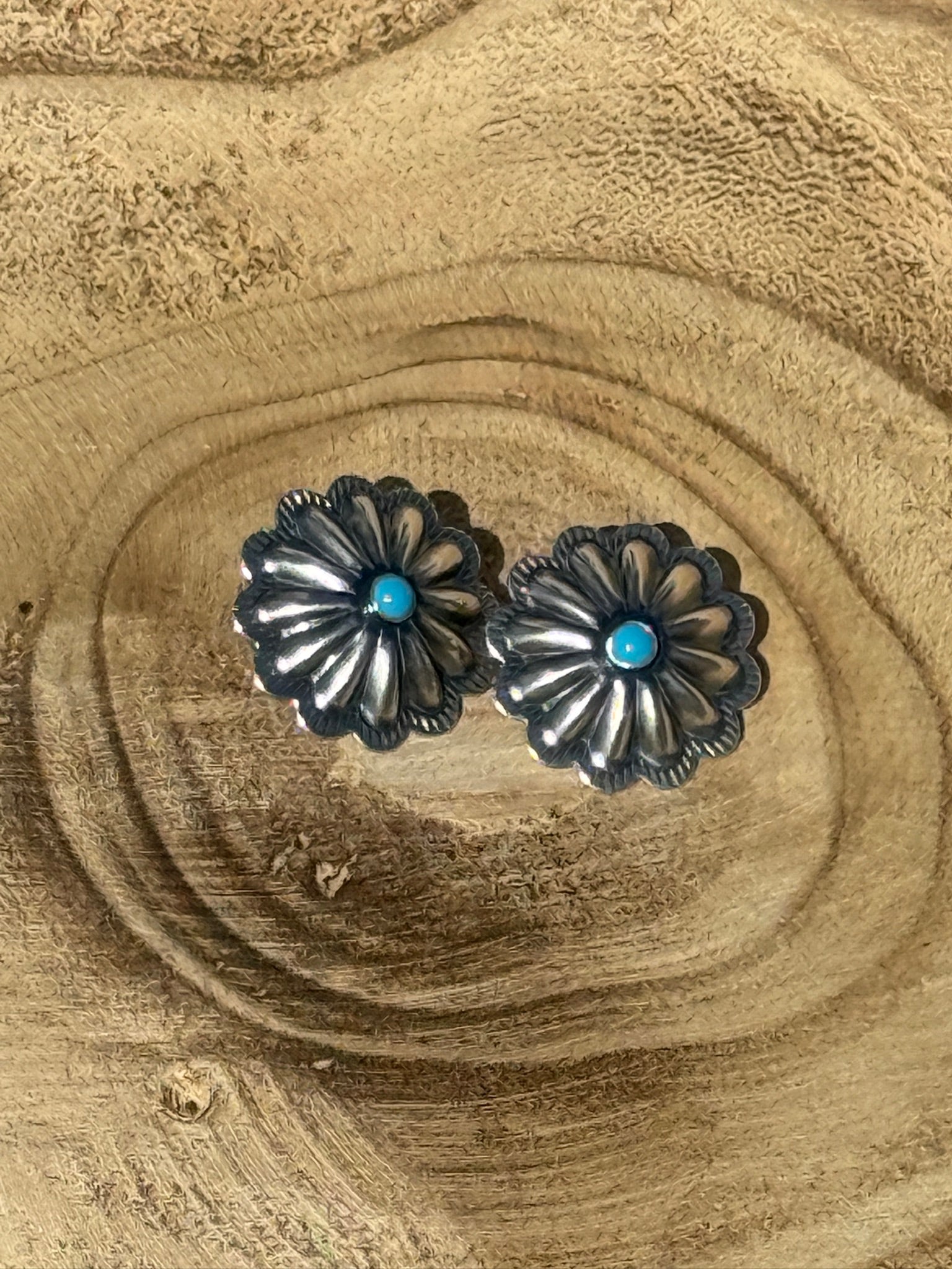 Pair of silver floral earrings with turquoise stones on a wooden surface