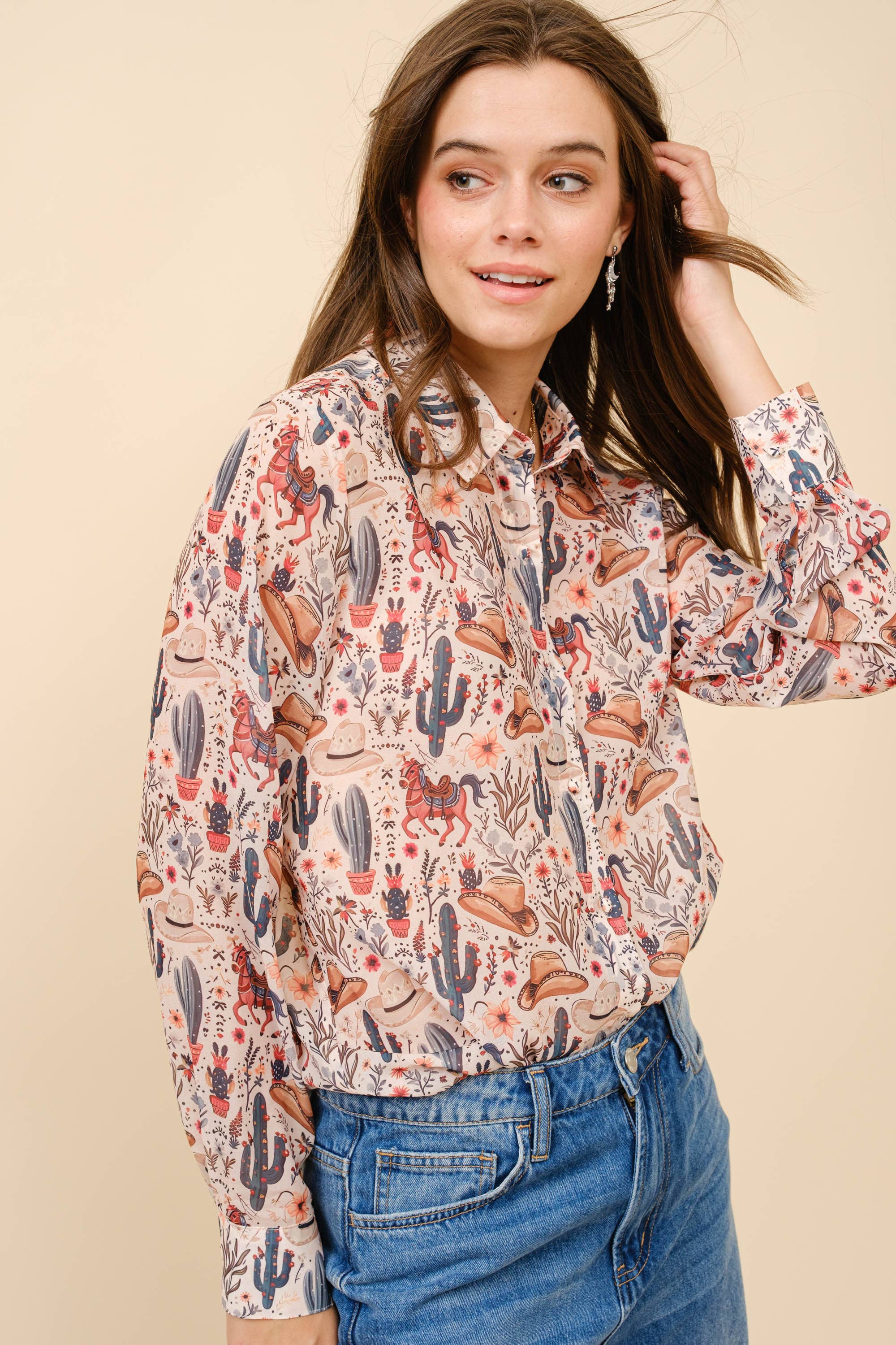 Woman wearing a patterned shirt with long sleeves and jeans against a beige background