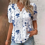 Woman wearing a white blouse with blue floral patterns against a wooden and brick wall.