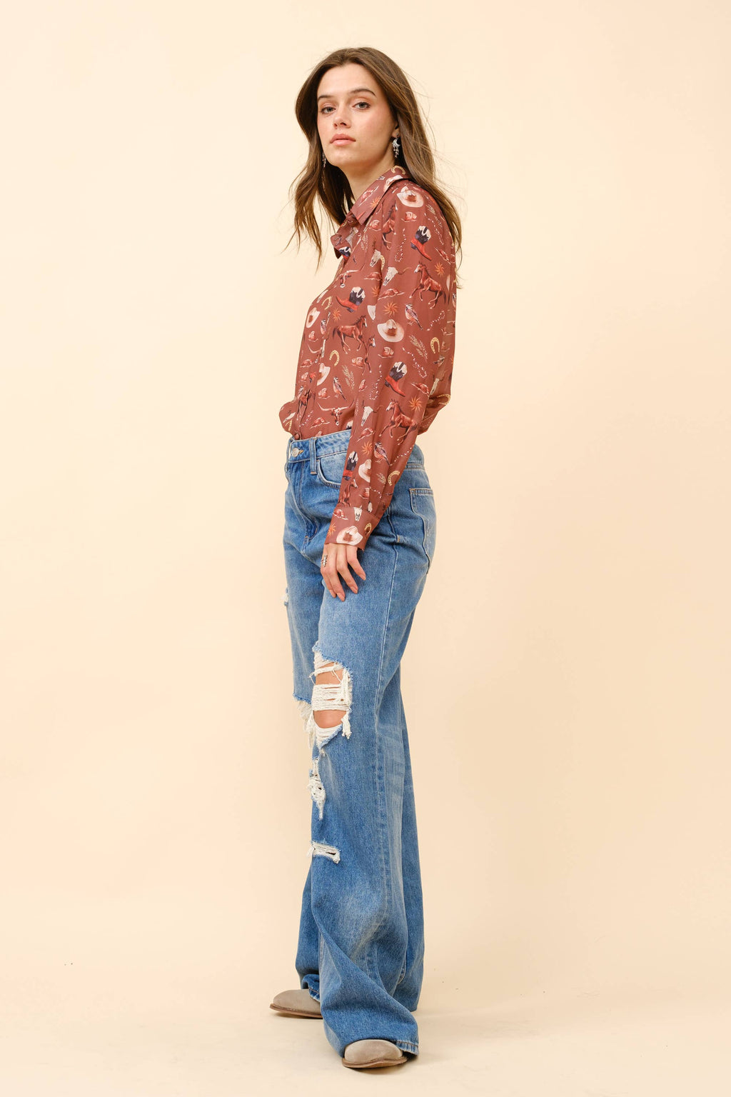Woman wearing a patterned blouse and blue jeans on a beige background