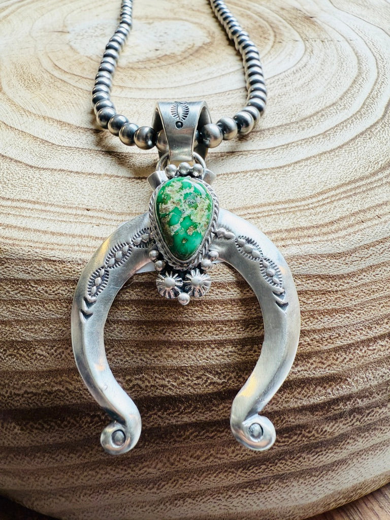 Silver pendant with green stone on a wooden surface
