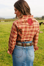 Person wearing a plaid shirt with floral embroidery in a grassy field