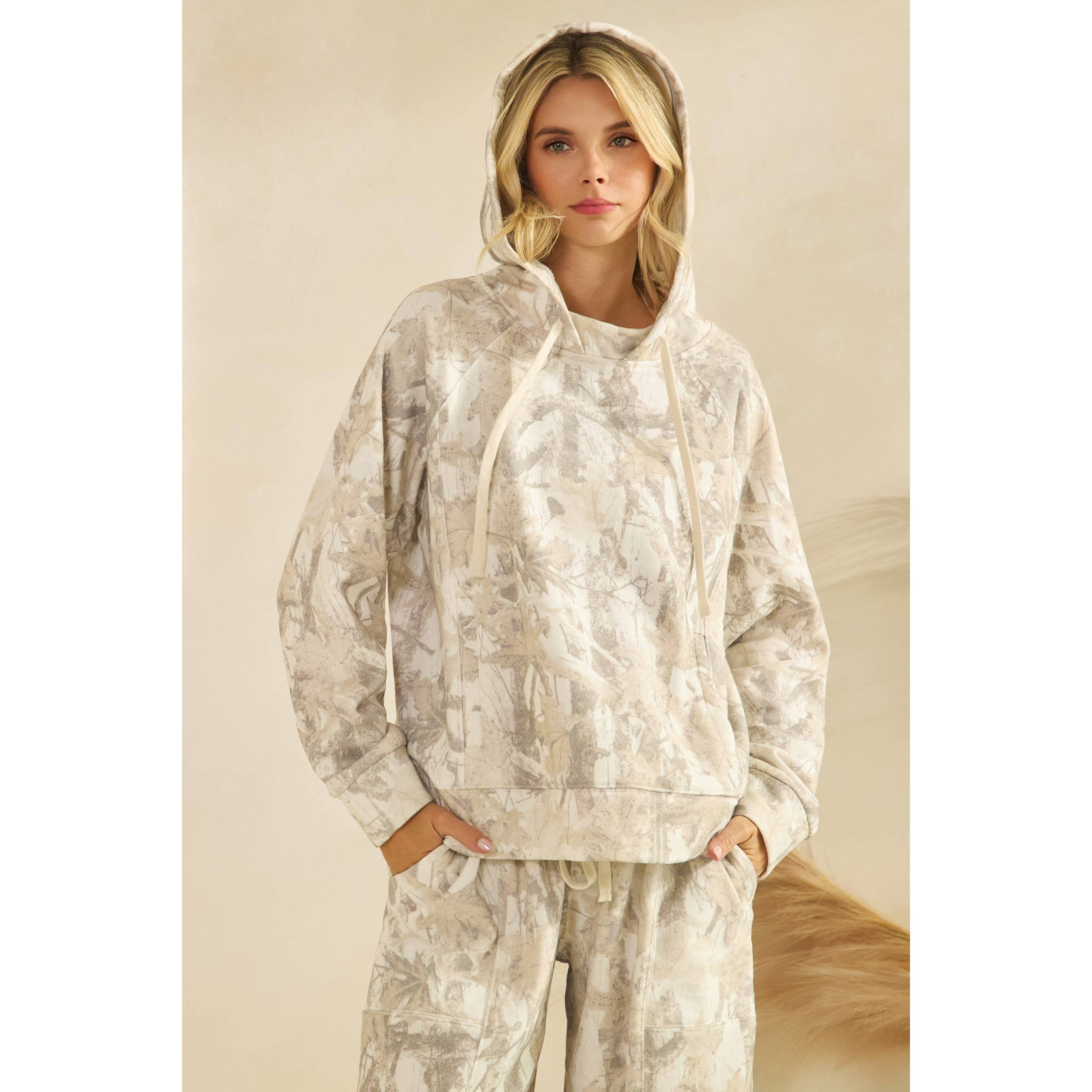 Woman wearing a beige tie-dye hoodie and pants on a plain background