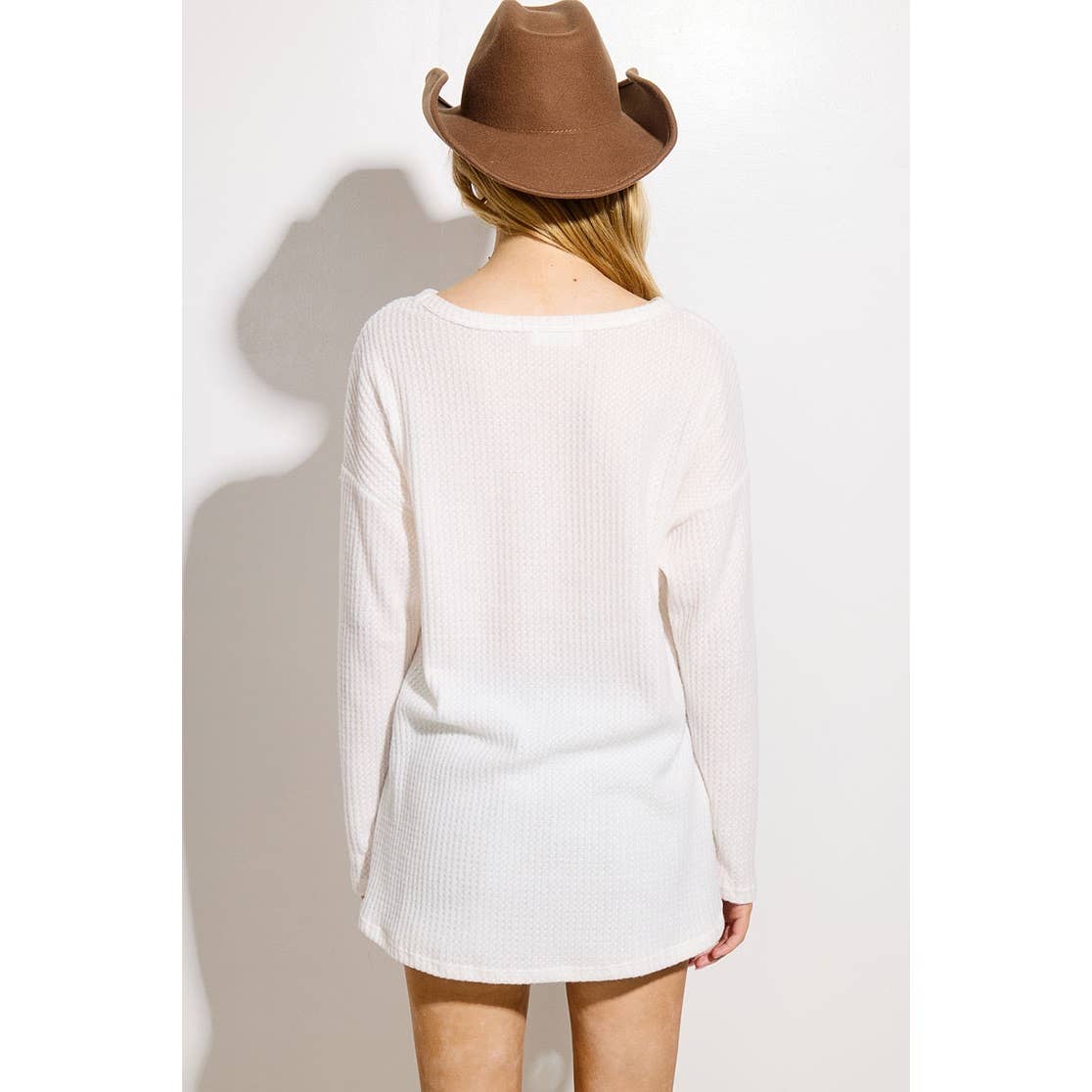 Person wearing a white sweater and brown hat on a plain background