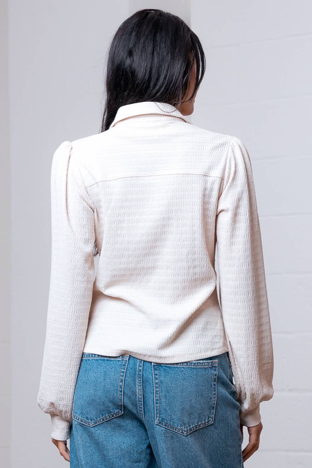 Person wearing a cream-colored textured shirt and blue jeans against a plain background