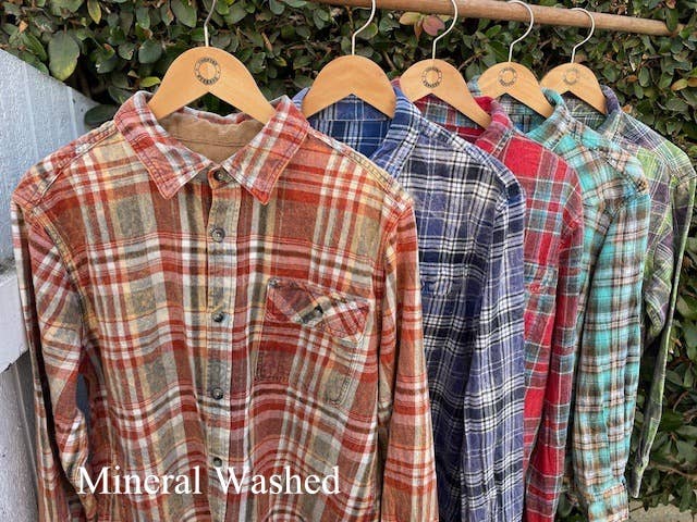 Plaid shirts on hangers with 'Mineral Washed' text against a natural background