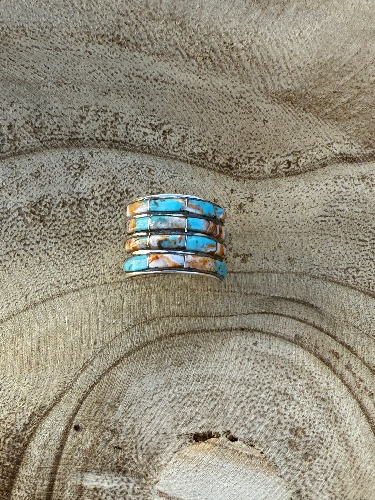 Stack of turquoise and silver rings on a textured beige surface