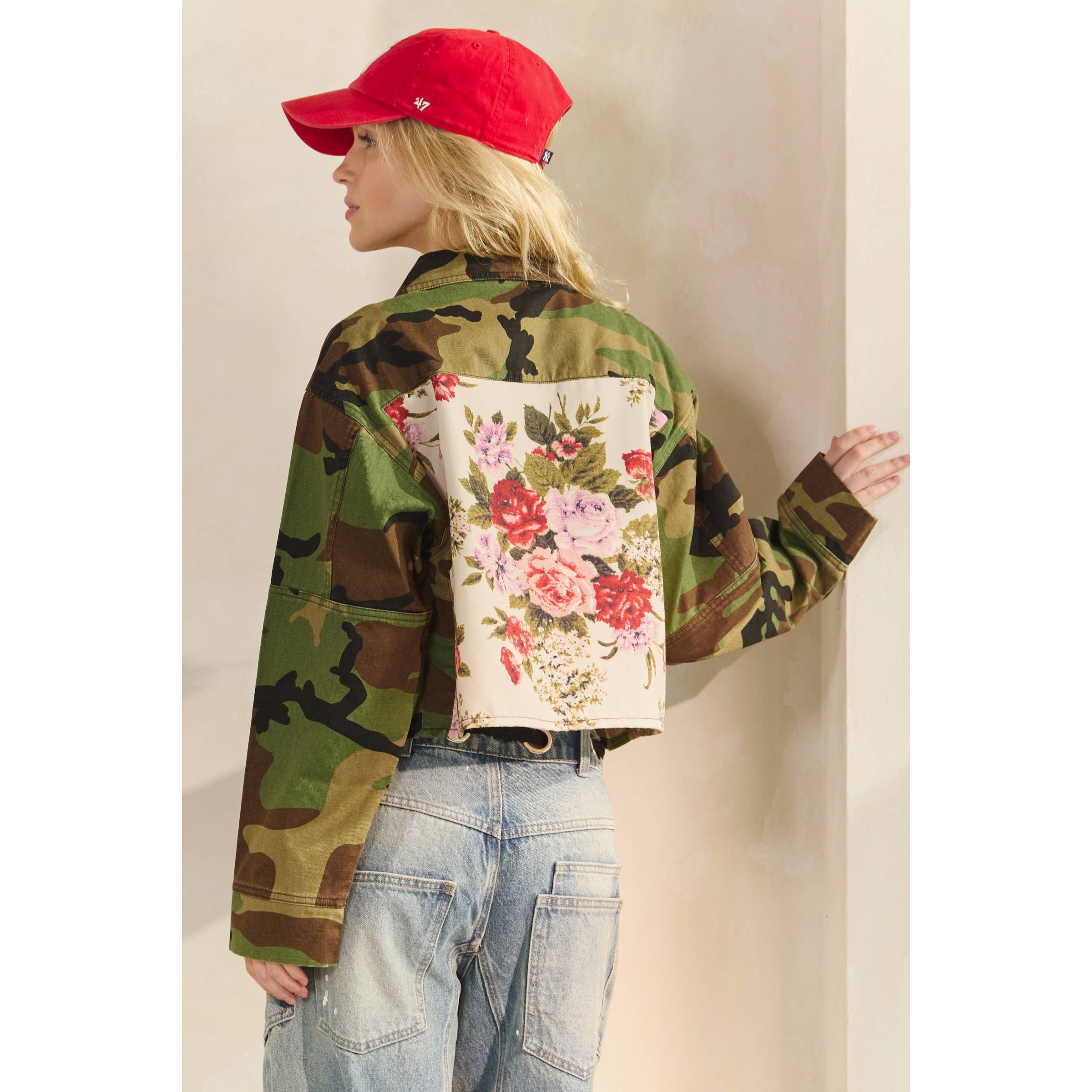 Person wearing a camouflage jacket with floral back panel and red cap.