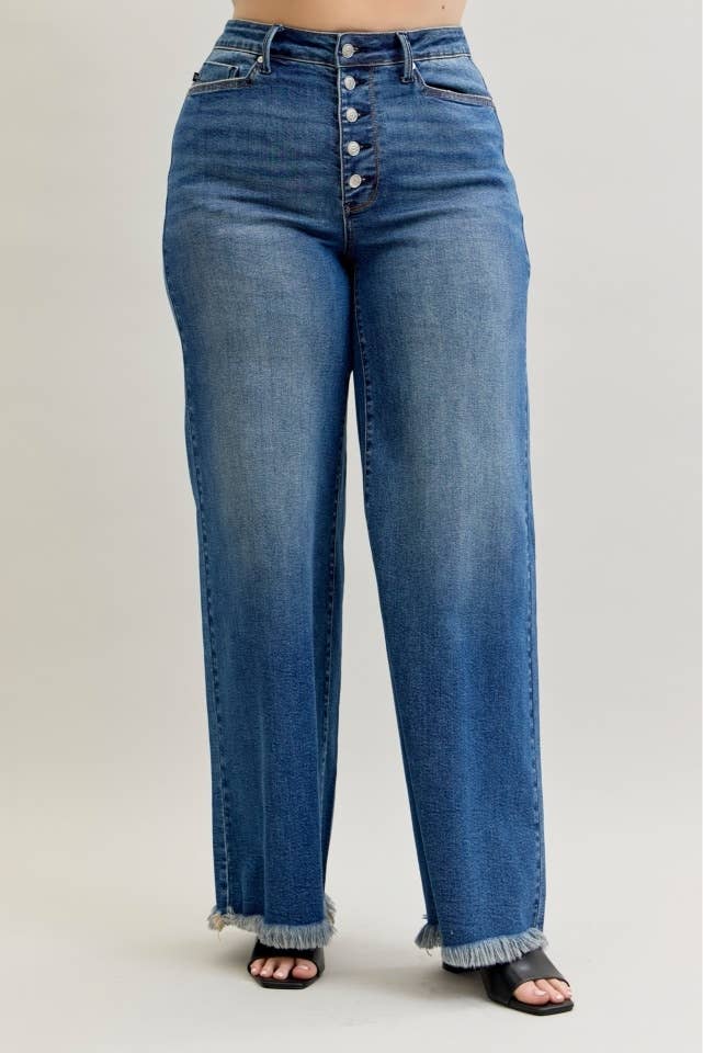A person wearing medium-wash blue denim jeans with a high waist, front button closure, and wide legs with frayed hems, shown against a plain light gray studio background.