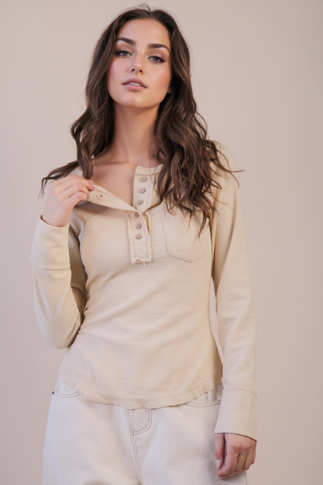 Woman wearing a beige long-sleeve top with buttons against a plain background