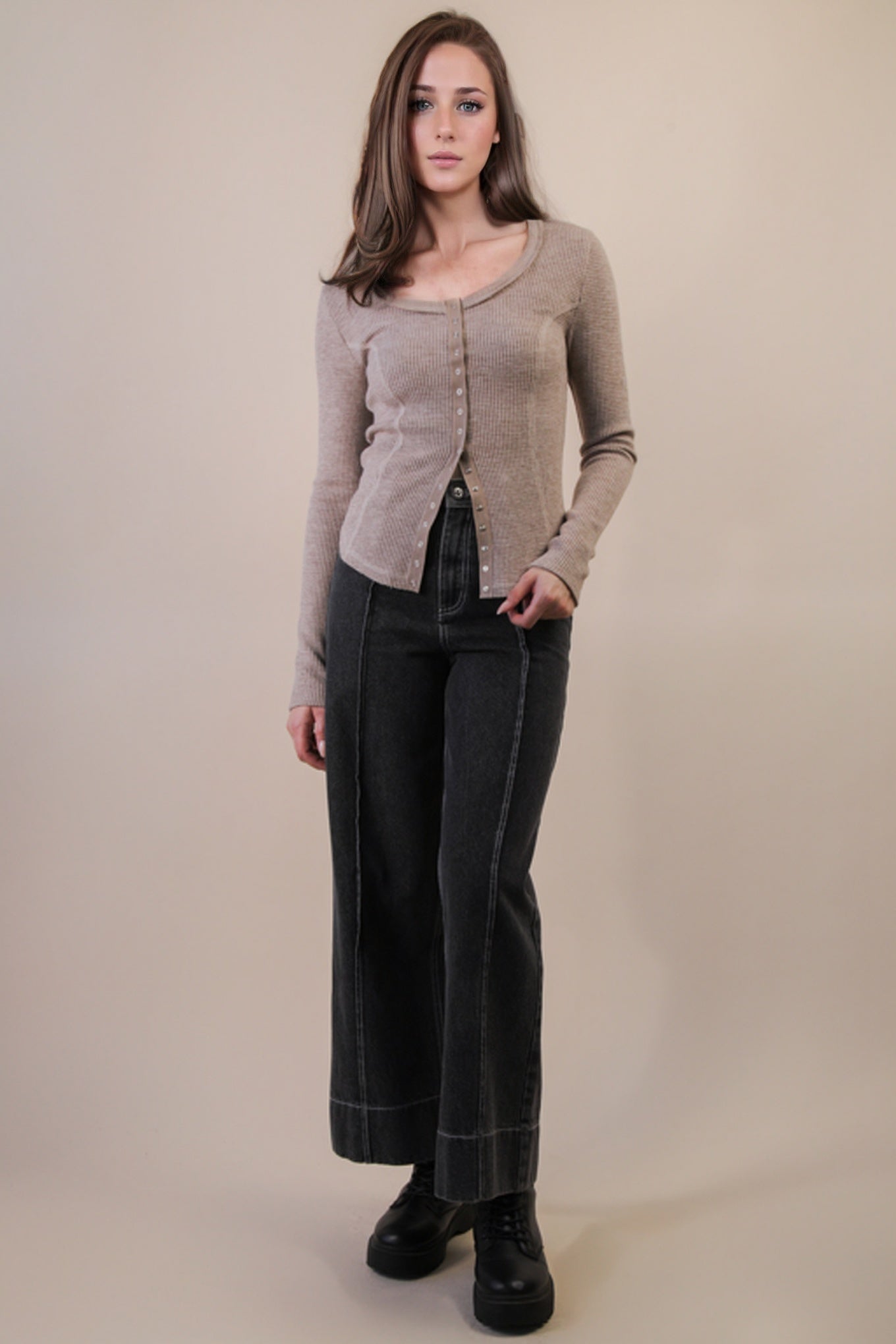 Woman wearing a beige cardigan and dark pants against a beige background