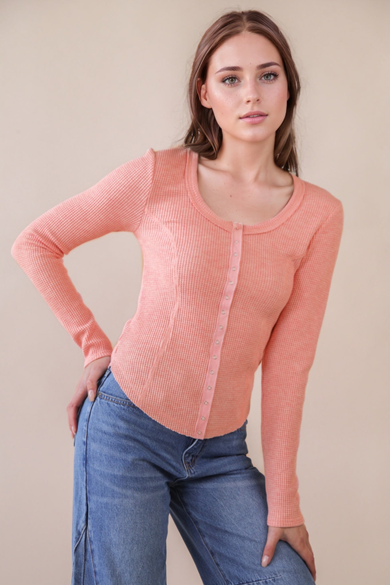 Woman wearing a pink long-sleeve top and blue jeans against a beige background