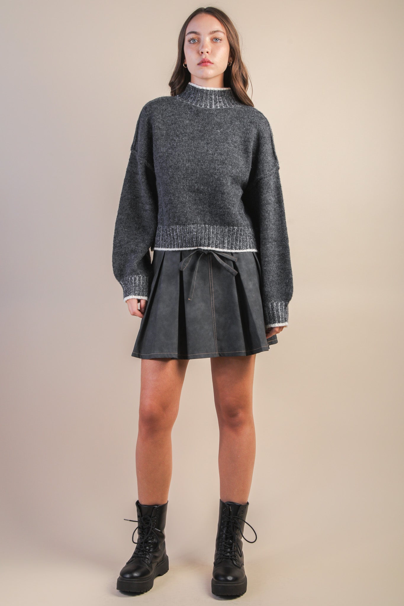 Woman wearing a gray sweater and black skirt against a beige background