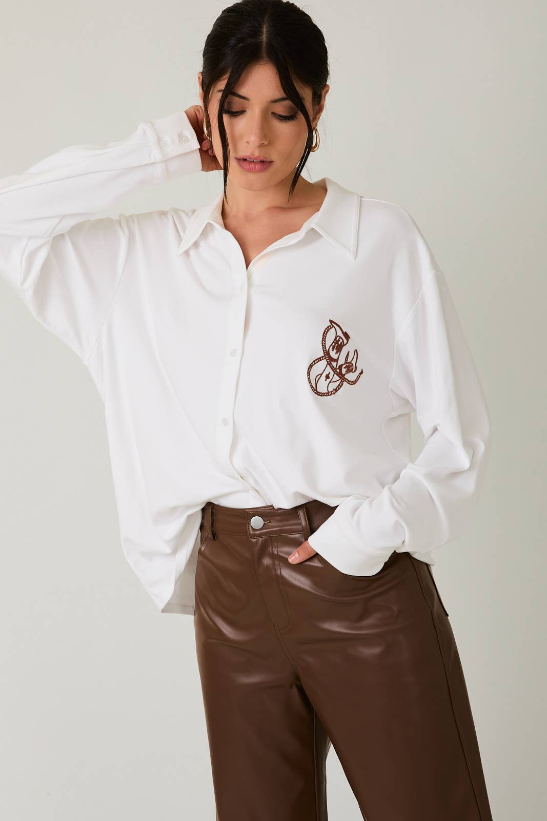 Woman wearing a white blouse with embroidery and brown pants on a plain background