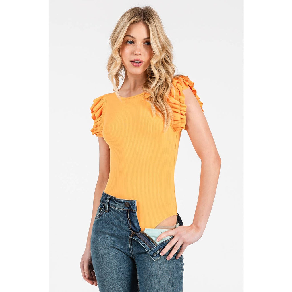 Woman wearing a yellow top with ruffled sleeves and blue jeans on a white background