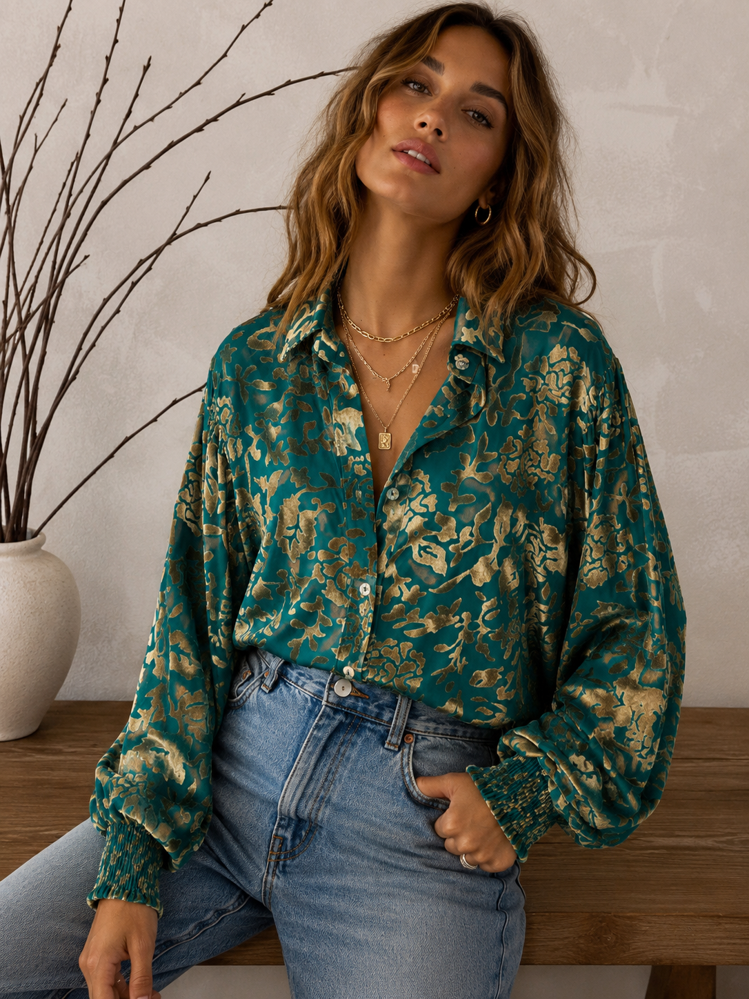 Woman wearing a green floral blouse and blue jeans against a neutral background