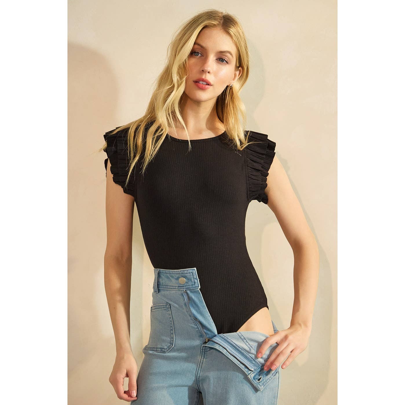 Woman wearing a black ruffled top and blue jeans against a beige background