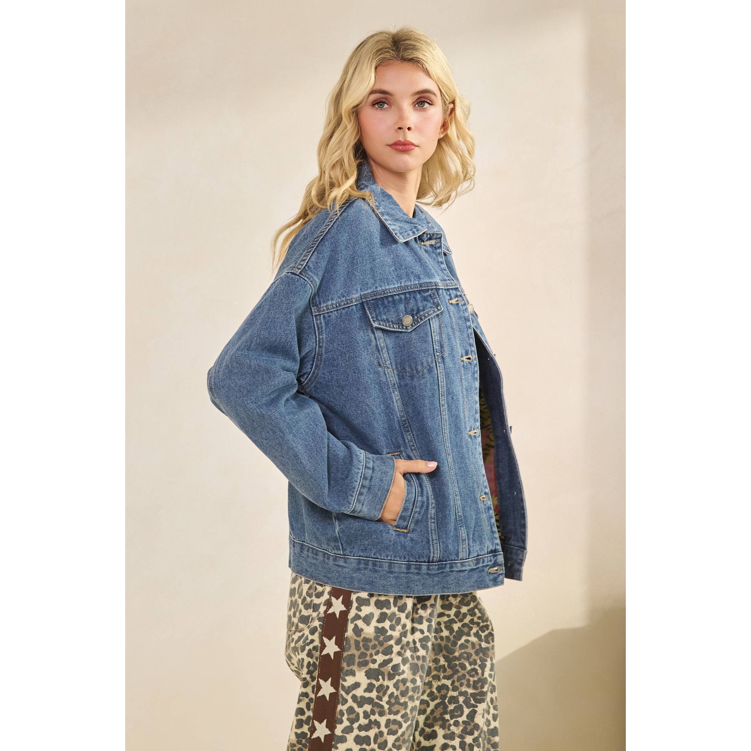 Woman wearing a blue denim jacket and leopard print pants against a beige background