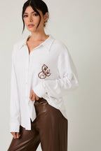 Woman wearing a white blouse with embroidery and brown pants on a plain background