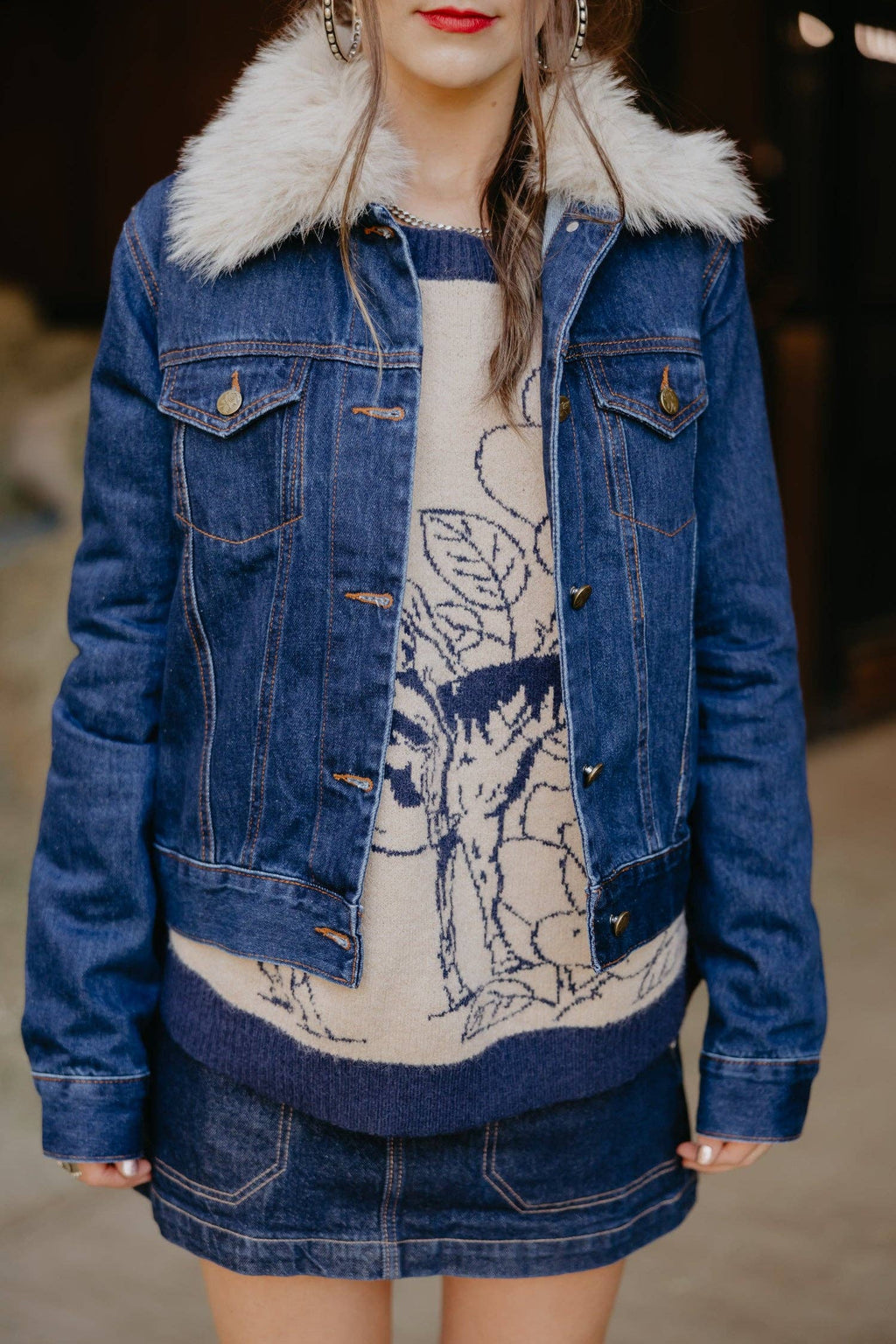 Person wearing a blue denim jacket with white fur collar and a patterned dress underneath.