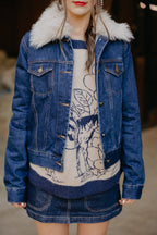 Person wearing a blue denim jacket with white fur collar and a patterned dress underneath.