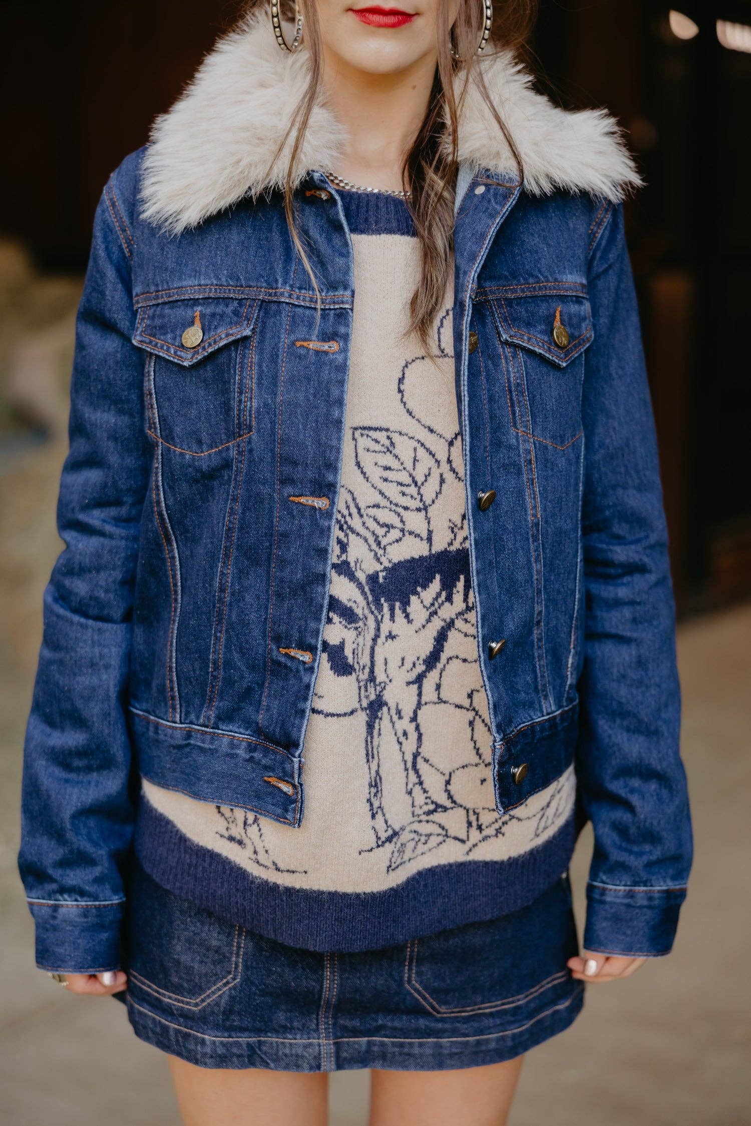 Person wearing a blue denim jacket with white fur collar and a patterned dress underneath.