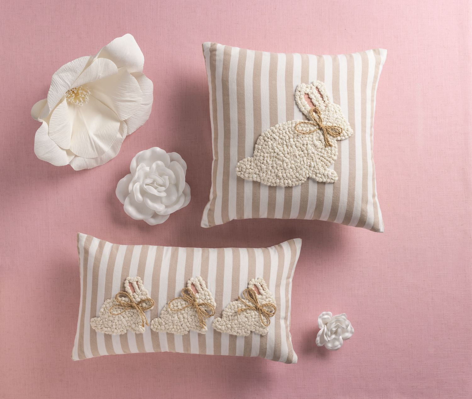 Two striped pillows with embroidered bunny designs on a pink background